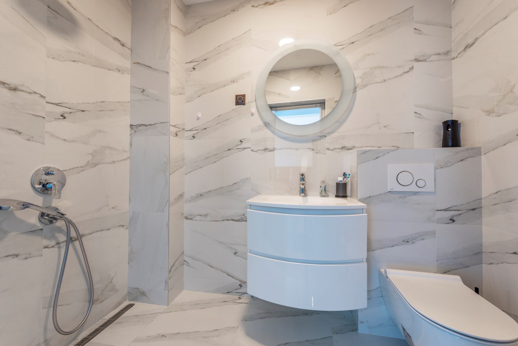 Modernes Badezimmer im Penthouse in Bečići, Montenegro: Marmoroptik, Dusche, runder Spiegel und Waschtisch.