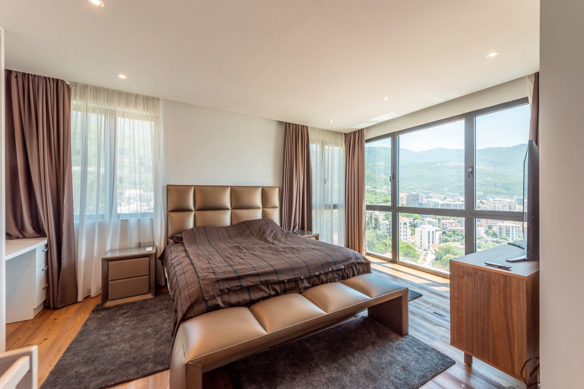 Schlafzimmer im Penthouse in Bečići, Montenegro: Doppelbett, Panoramafenster mit Blick auf die Berge und die Stadt.