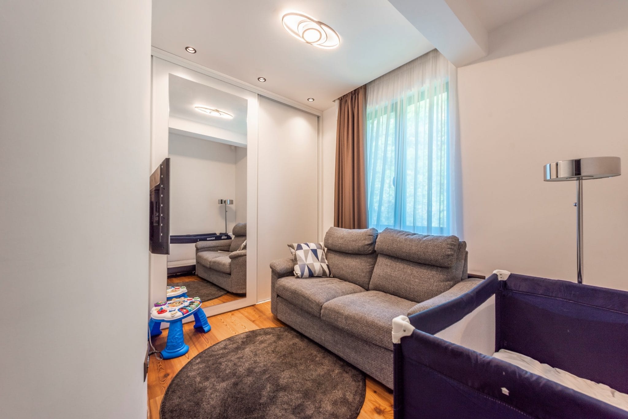 Wohnzimmer im Penthouse in Bečići, Montenegro: graues Sofa, verspiegelter Kleiderschrank, Kinderbett und Parkettboden.