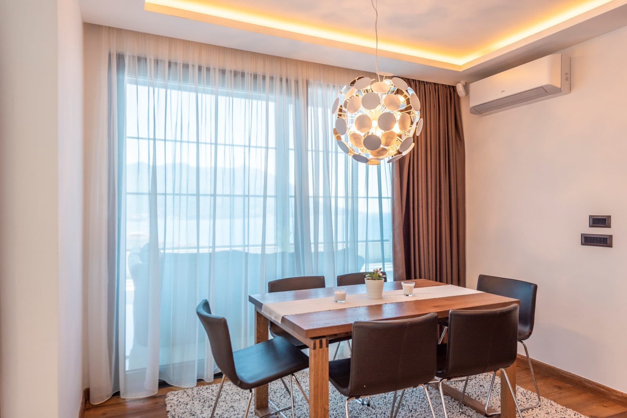 Essbereich im Penthouse in Bečići, Montenegro: Holztisch, Designerleuchte und Panoramafenster.