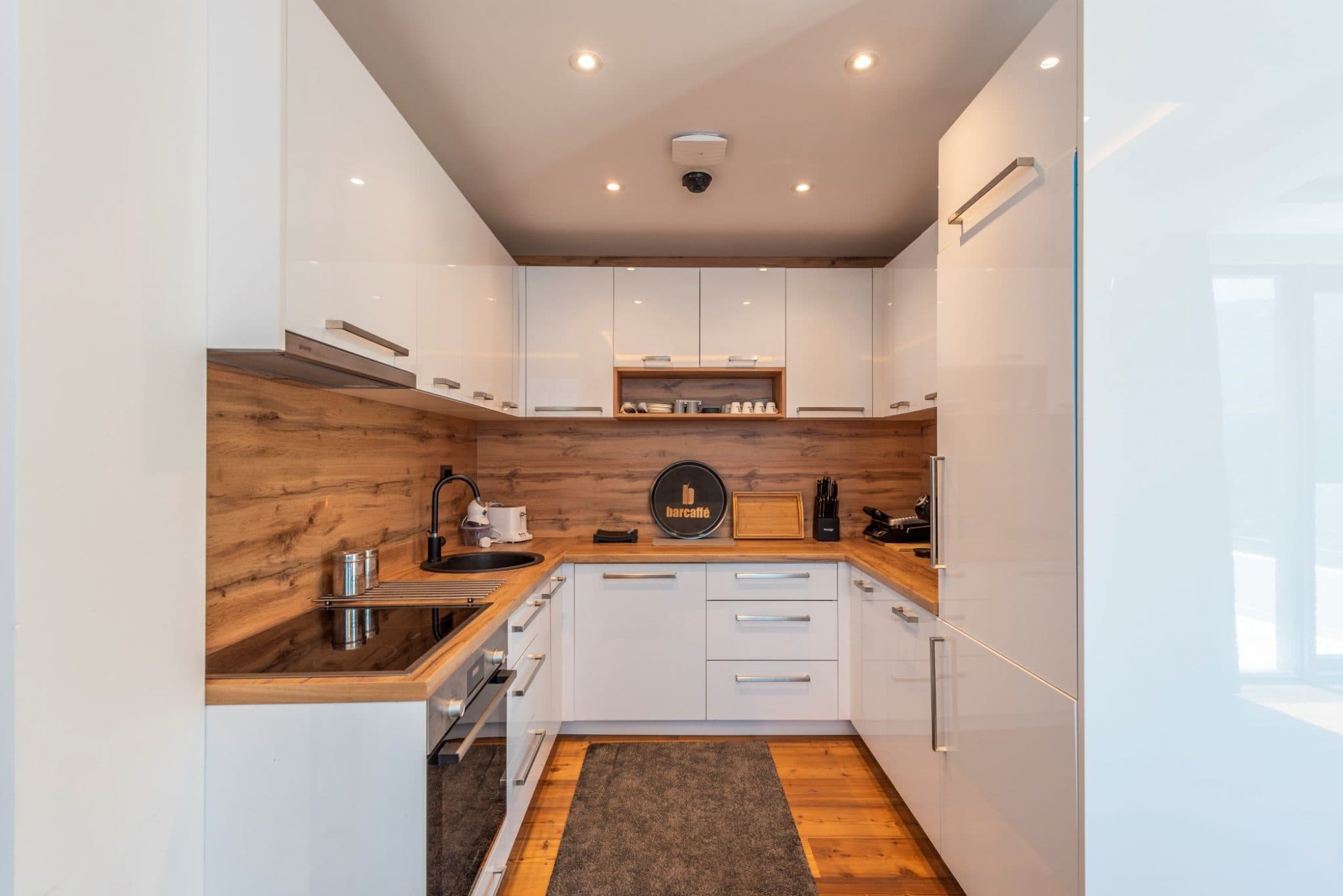 Moderne weiße Küche mit Holzverkleidung im Penthouse in Bečići, Montenegro: Einbaugeräte und stilvolles Design.