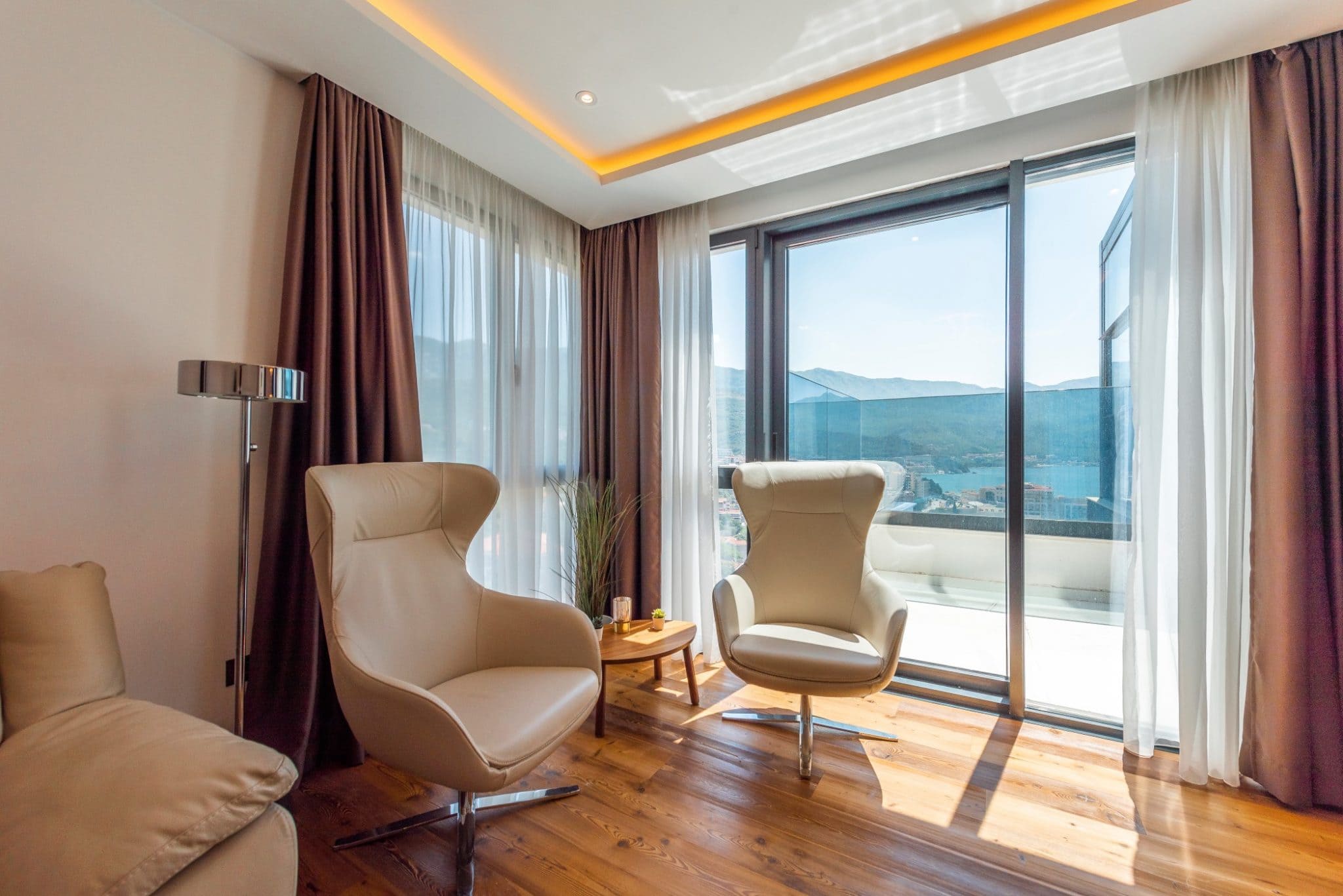 Wohnzimmer im Penthouse in Bečići, Montenegro: Ledersessel, Panoramafenster mit Blick auf das Meer und die Berge, modernes Design.