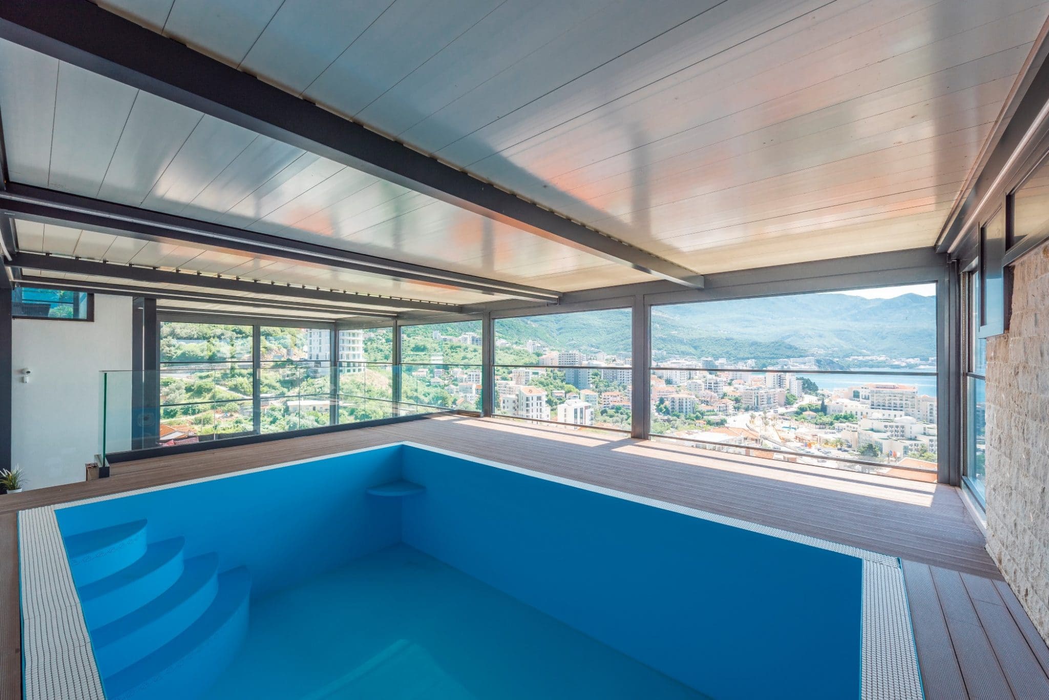 Überdachter Pool im Penthouse in Bečići, Montenegro, mit Panoramablick auf die Stadt, das Meer und die Berge durch Glaswände.