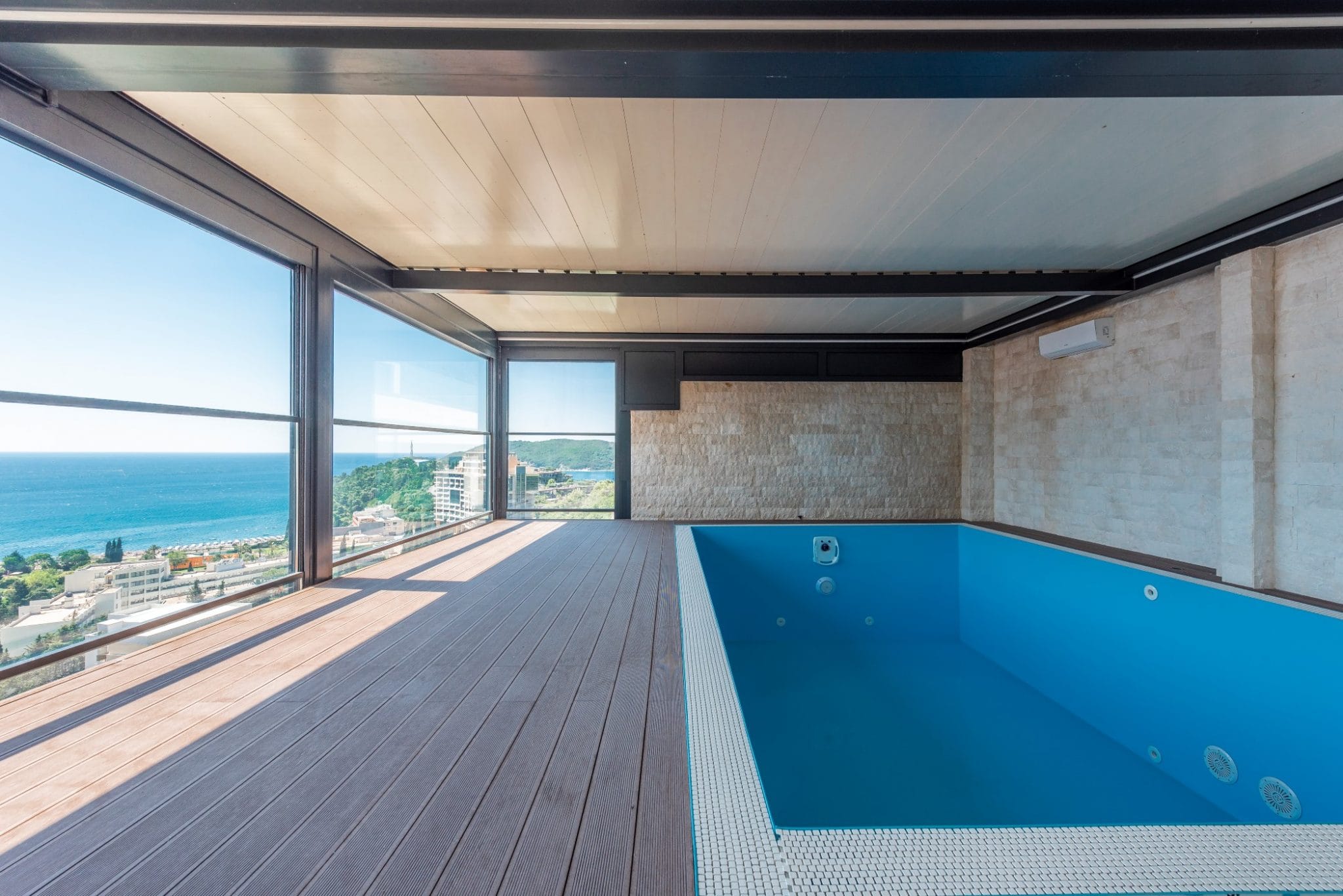 Überdachter Pool im Penthouse in Bečići, Montenegro: Panoramablick auf das Meer, Terrasse mit Holzdeck und Steinverkleidung.