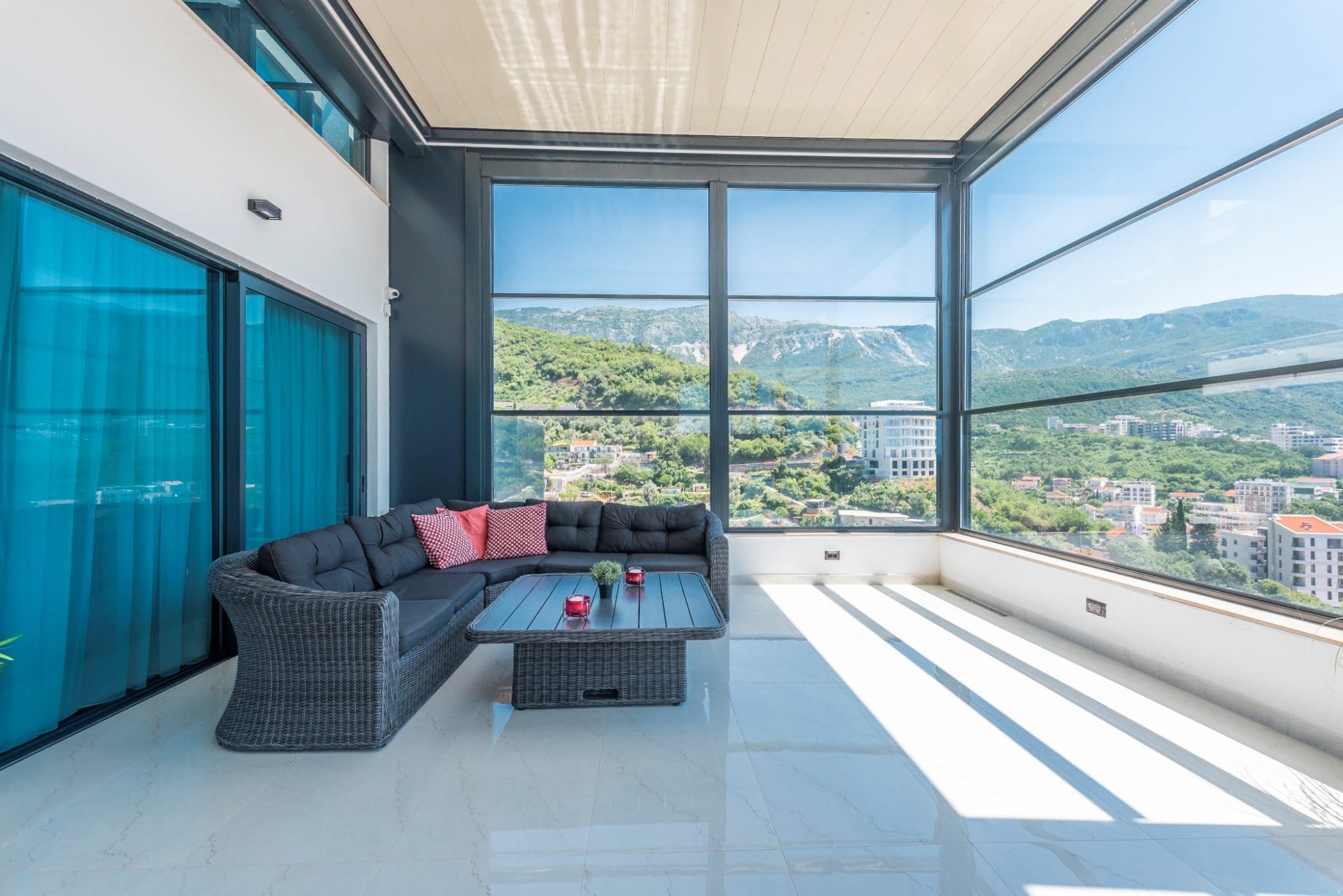 Panoramaterrasse des Penthouses in Bečići, Montenegro: geflochtene Möbel, heller Boden und Blick auf Berge und Stadt.