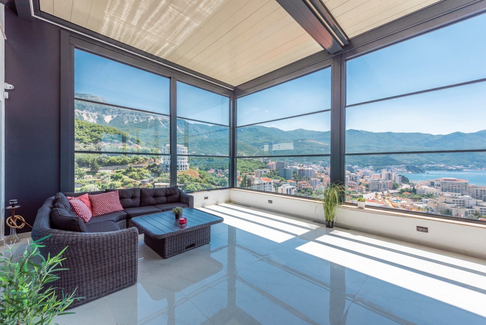Panoramaterrasse des Penthouses in Bečići, Montenegro: Rattanmöbel, Panoramaverglasung und Blick auf das Meer und die Berge.