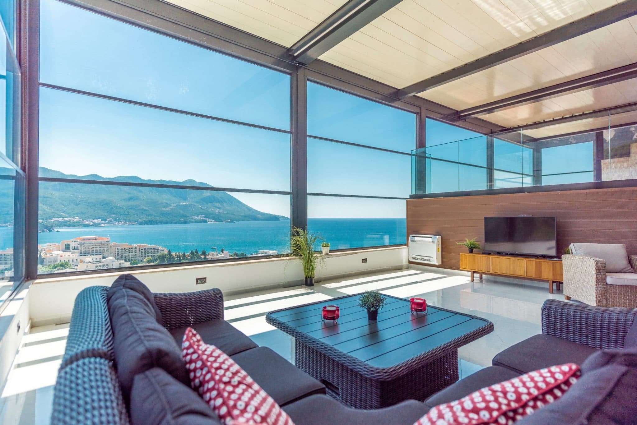 Wohnzimmer im Penthouse in Bečići, Montenegro: Panoramaverglasung, Meerblick, Rattanmöbel und Terrasse.