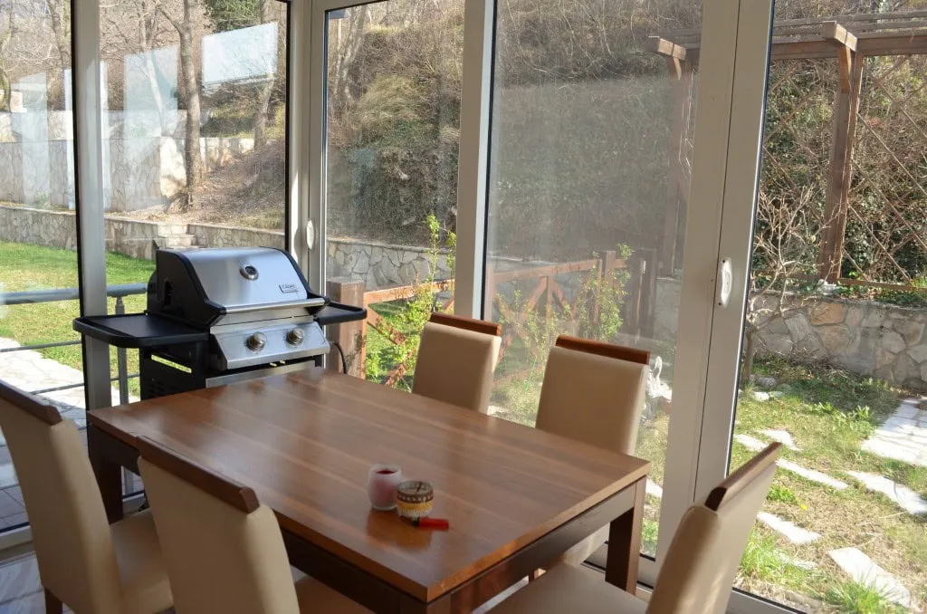 Essbereich mit Grill im Wohnzimmer eines Apartments in Bar, Montenegro, mit Panoramafenstern und Blick auf den Garten.