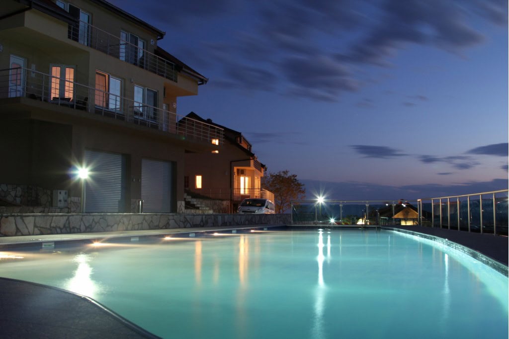 Karadağ’ın Bar şehrindeki modern villanın aydınlatmalı akşam havuzu, teraslı dairelere bakış.