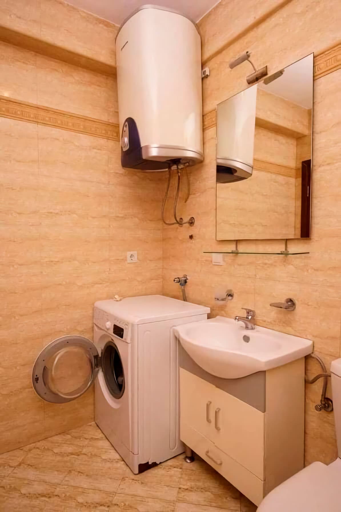 Badezimmer in einer Wohnung in Budva, Montenegro: beige Fliesen, Waschmaschine, Waschbecken mit Unterschrank und Boiler.