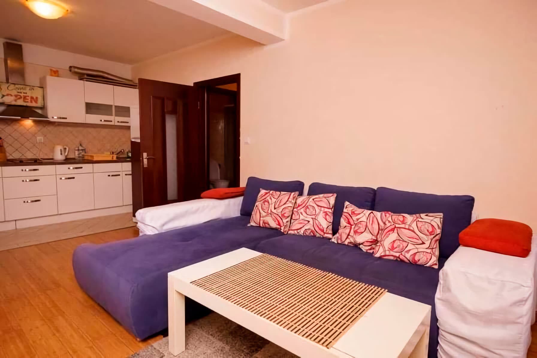 Wohnzimmer mit blauem Ecksofa und Küche in einer Wohnung, Budva, Montenegro. Modernes Interieur mit weißen Möbeln.