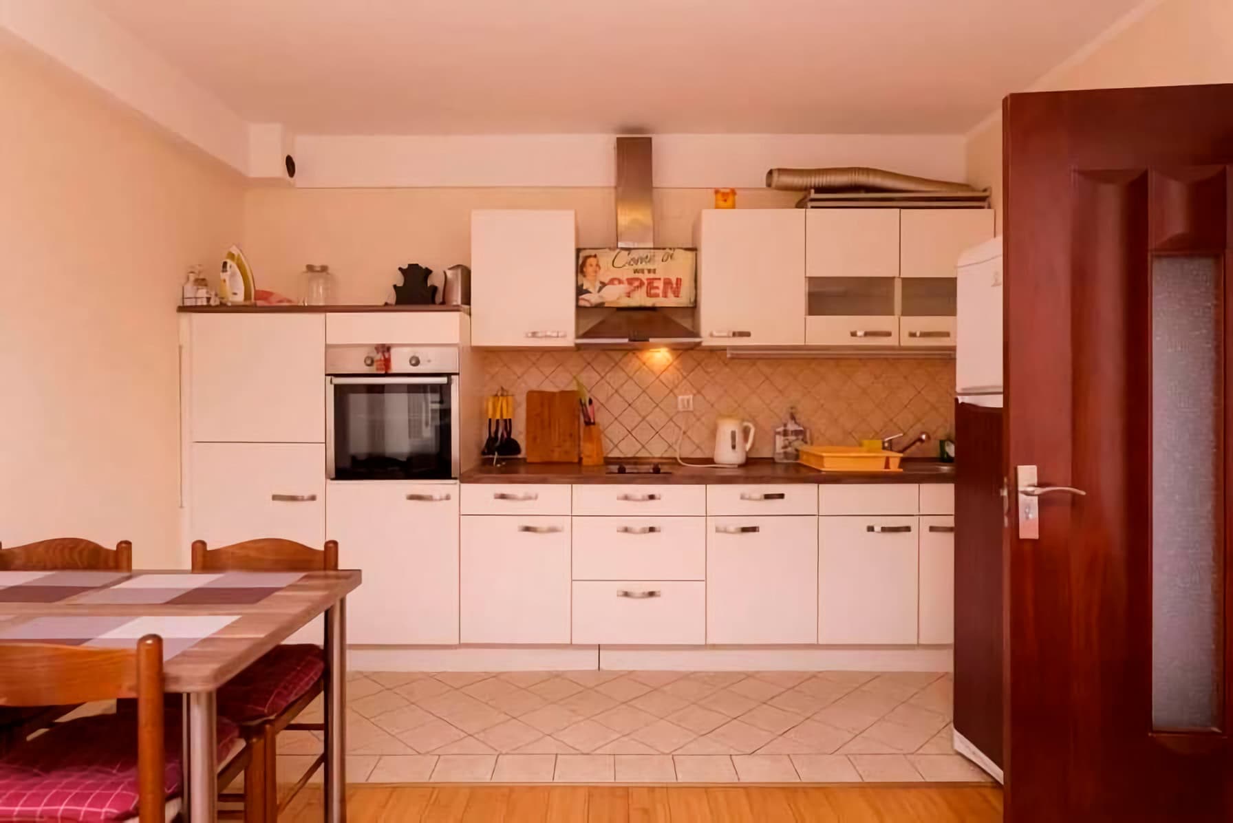 Helle Küche mit weißer Einbauküche und Essbereich in einer Wohnung in Budva, Montenegro. Gemütliches Interieur mit Fliesenboden.