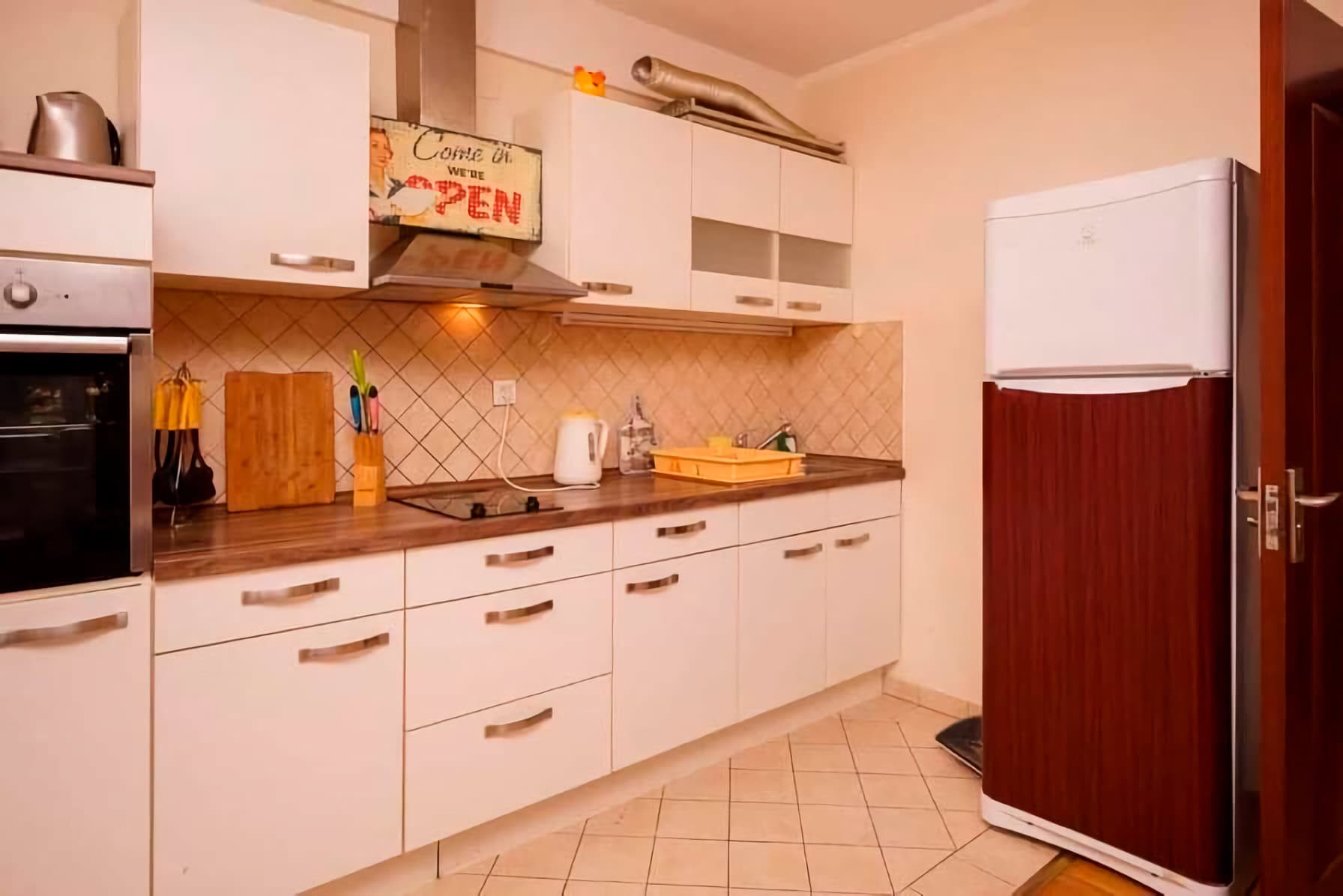 Helle Küche in einer Wohnung in Budva, Montenegro: weiße Fronten, Einbaugeräte, gefliester Spritzschutz und Kühlschrank.