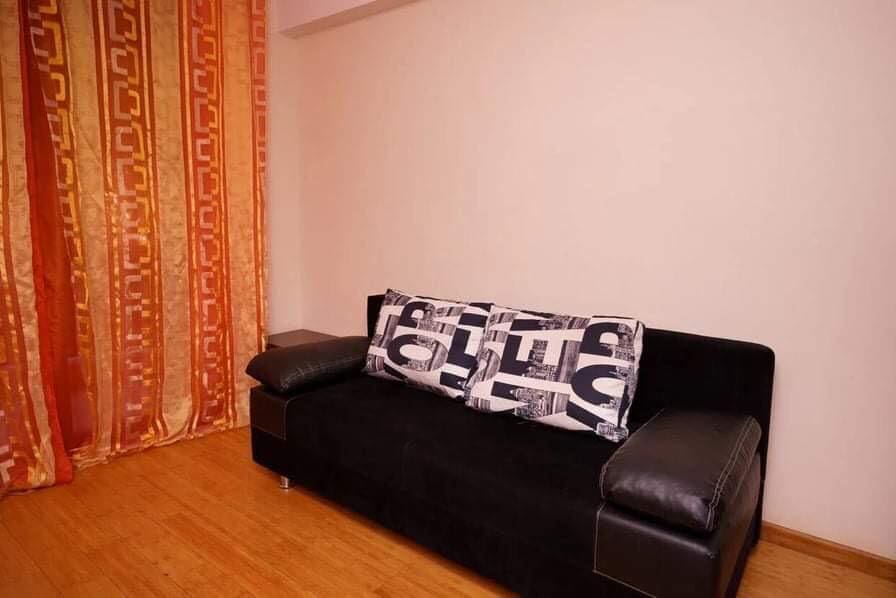 Wohnzimmer mit schwarzem Sofa und hellen Vorhängen in einer zum Verkauf stehenden Wohnung in Budva, Montenegro. Helles Interieur mit Laminatboden.