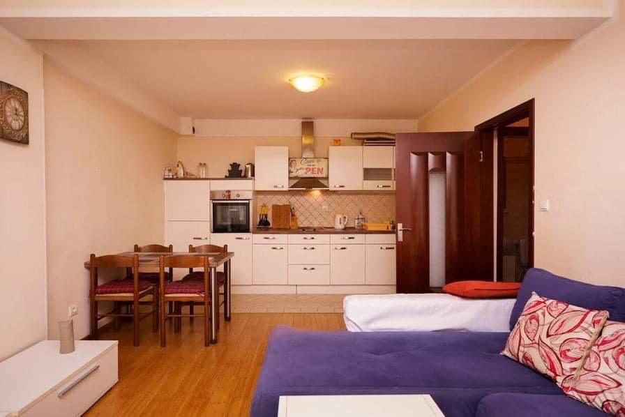 Wohnzimmer mit Küche in einer Wohnung in Budva, Montenegro: helle Küchenzeile, Essbereich und violettes Ecksofa.