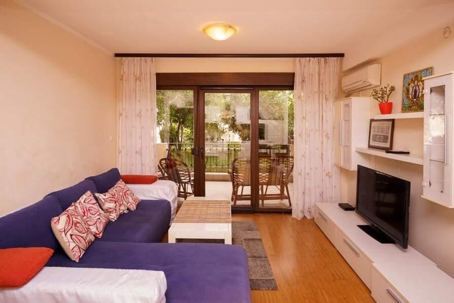 Gemütliches Wohnzimmer mit blauem Sofa und Zugang zur Terrasse in einer Wohnung in Budva, Montenegro: modernes Interieur mit TV-Bereich.