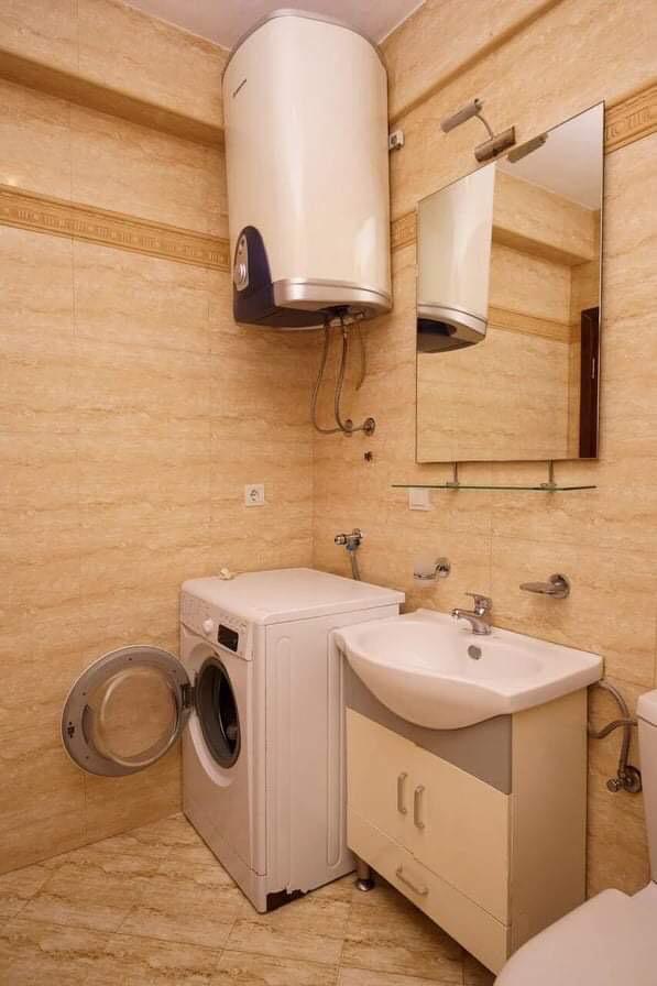 Badezimmer in einer Wohnung in Budva, Montenegro: beige Fliesen, Waschmaschine, Boiler und Waschtischunterschrank mit Waschbecken.
