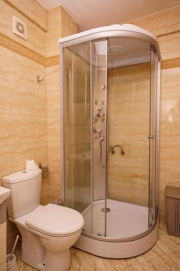 Badezimmer in einer Wohnung in Budva, Montenegro: weiße Duschkabine und Sanitäranlagen, Wände mit beigen Fliesen verkleidet.