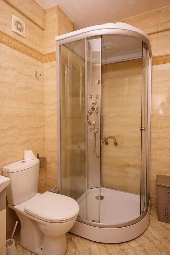 Kupatilo u stanu u Budvi, Crna Gora: bela tuš kabina i sanitarije, zidovi obloženi bež pločicama.