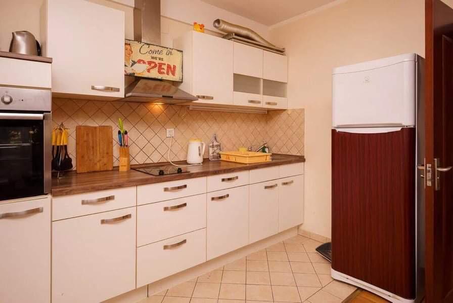 Helle Küche mit weißer Einbauküche, integrierten Geräten und Kühlschrank in einer zum Verkauf stehenden Wohnung in Budva, Montenegro.