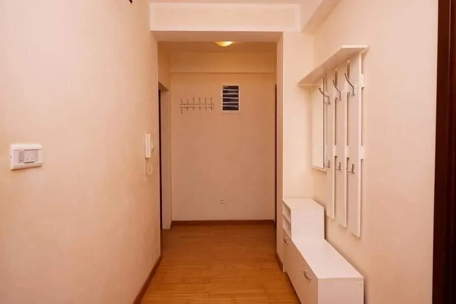 Svetao hodnik u stanu u Budvi, Crna Gora: beli nameštaj, vešalica za odeću i laminat na podu.