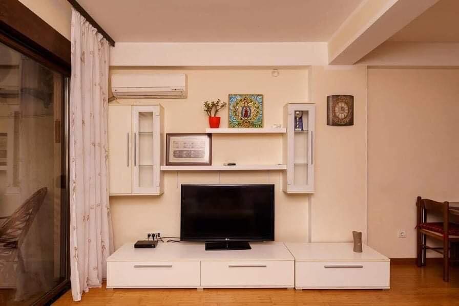 Wohnzimmer in einer Wohnung in Budva, Montenegro: weiße TV-Kommode, Wandregale, Klimaanlage und Zugang zum Balkon.