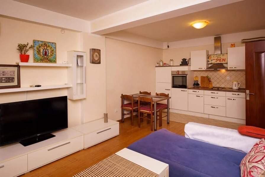 Wohnzimmer mit Küche in einer Wohnung in Budva, Montenegro: helle Möbel, Essbereich, TV-Bereich und Sofa im Interieur.