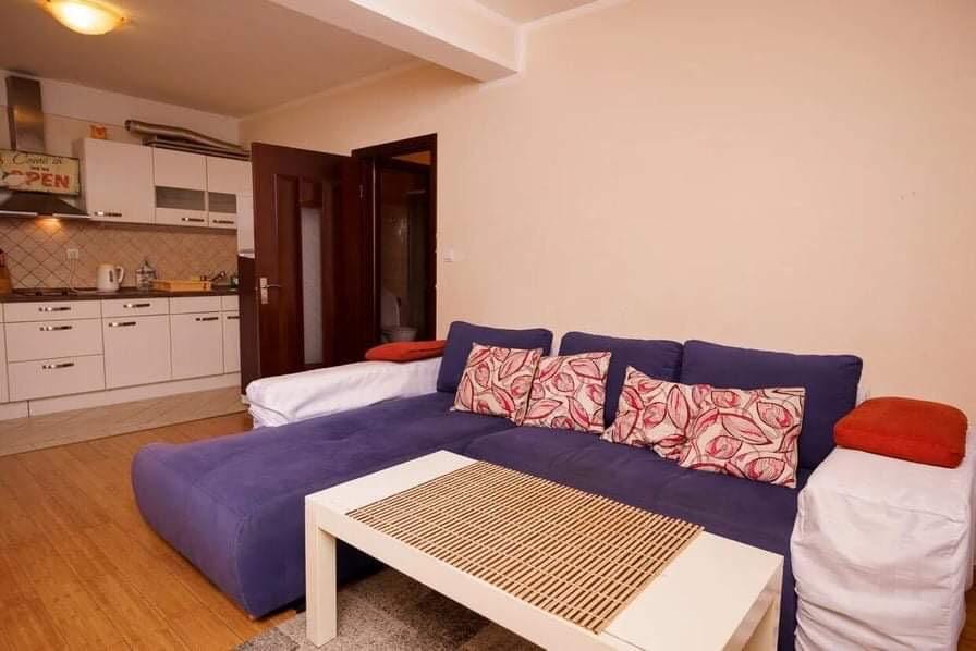 Wohnzimmer mit blauem Ecksofa und Küche in einer Wohnung, Budva, Montenegro. Modernes Interieur mit weißen Möbeln.