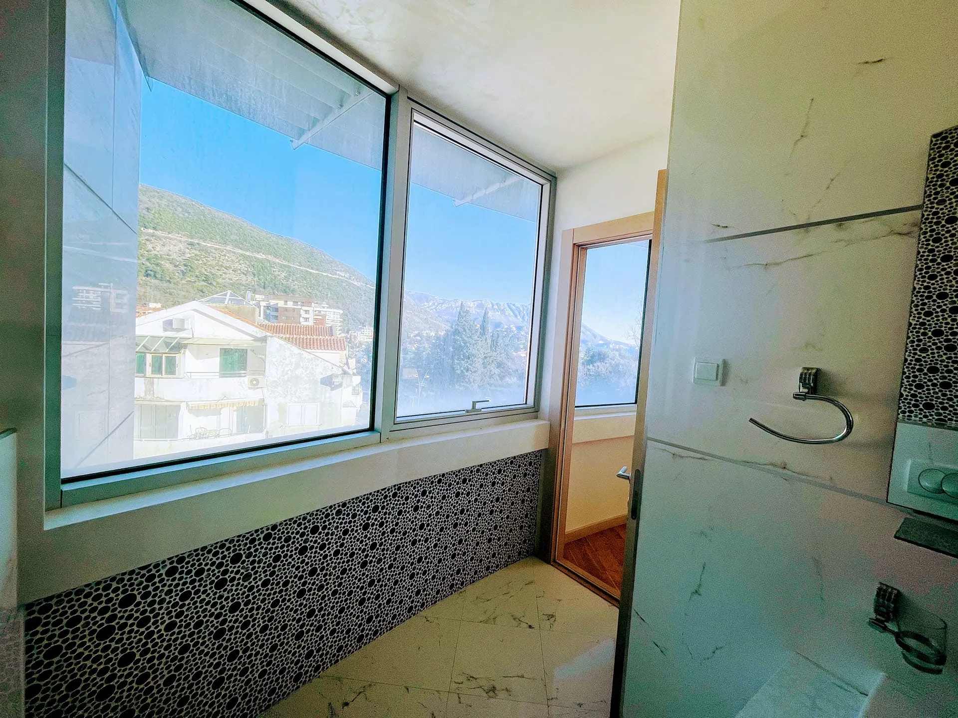 Badezimmer mit Panoramafenster und Bergblick in einer Wohnung in Budva, Montenegro: moderne Fliesen und Ausstattung.