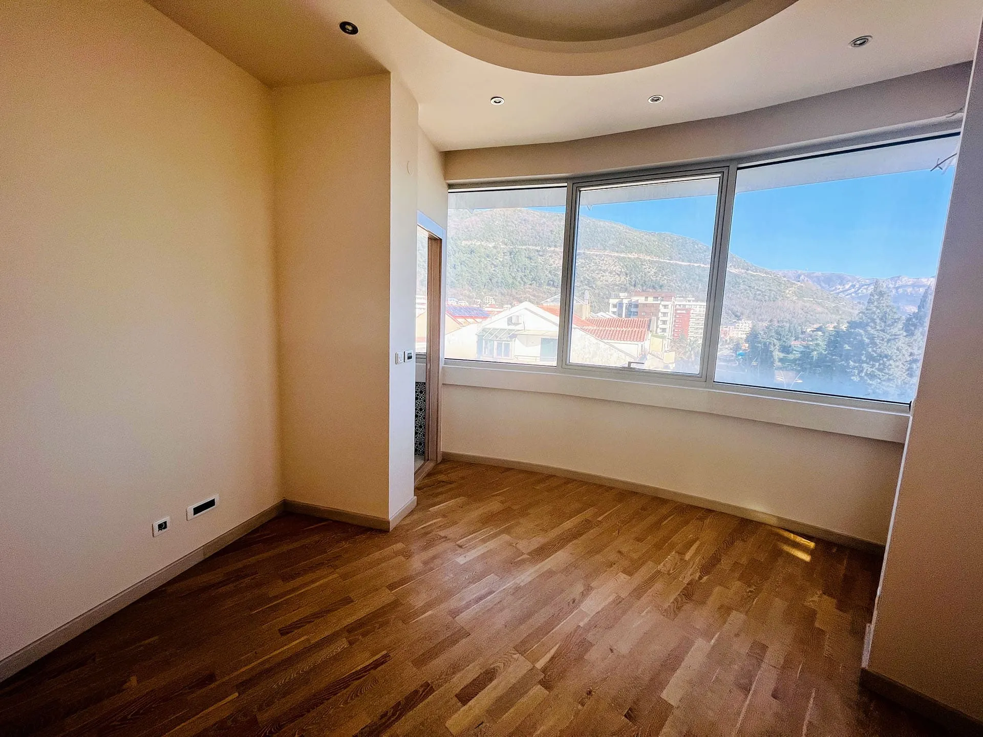 Helles Wohnzimmer mit Panoramafenstern und Bergblick in einer Wohnung, Budva, Montenegro, Parkettboden, Spotbeleuchtung.