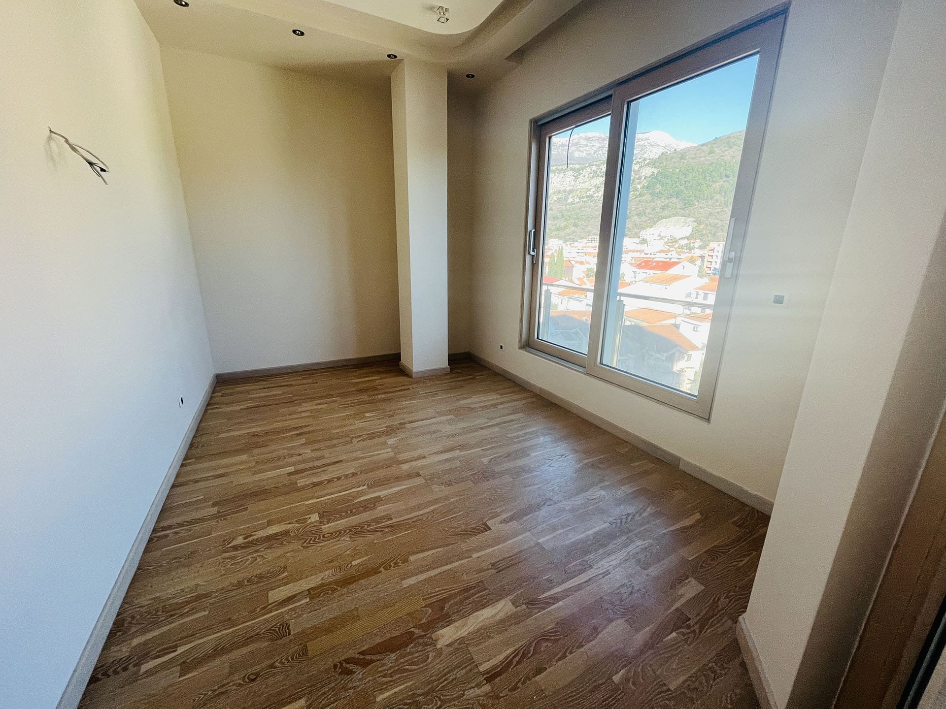 Helles Schlafzimmer mit Parkett und Panoramablick auf die Berge und die Stadt in einer neuen Wohnung, Budva, Montenegro.