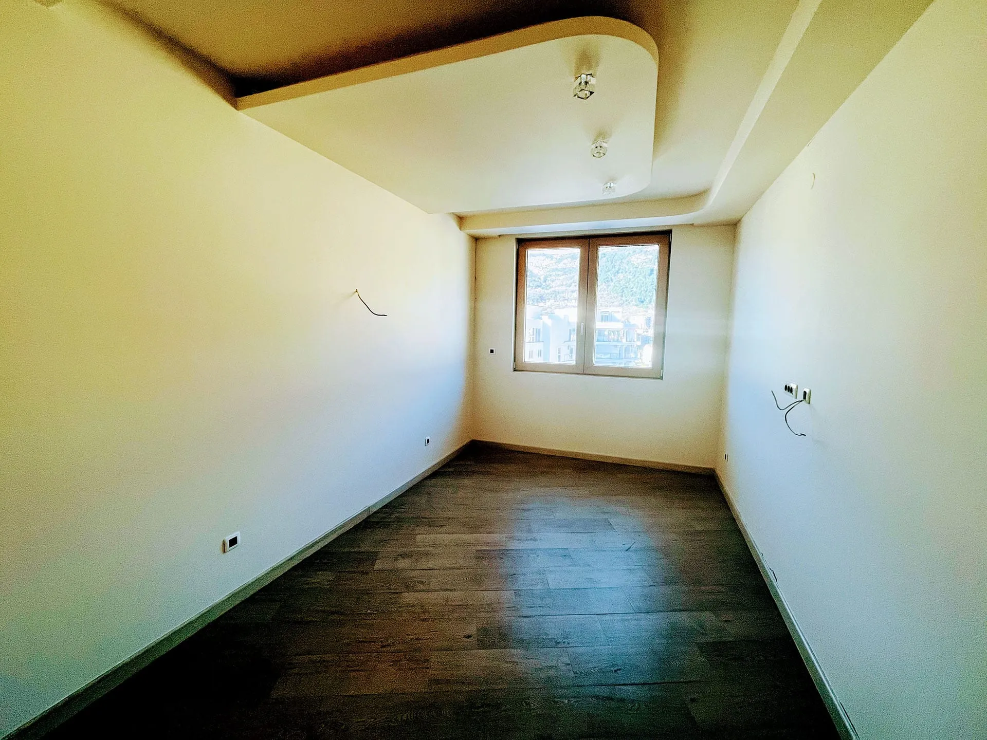 Helles Wohnzimmer in einer neuen Wohnung in Budva, Montenegro: Designer-Decke, dunkles Laminat und Ausblick aus dem Fenster.