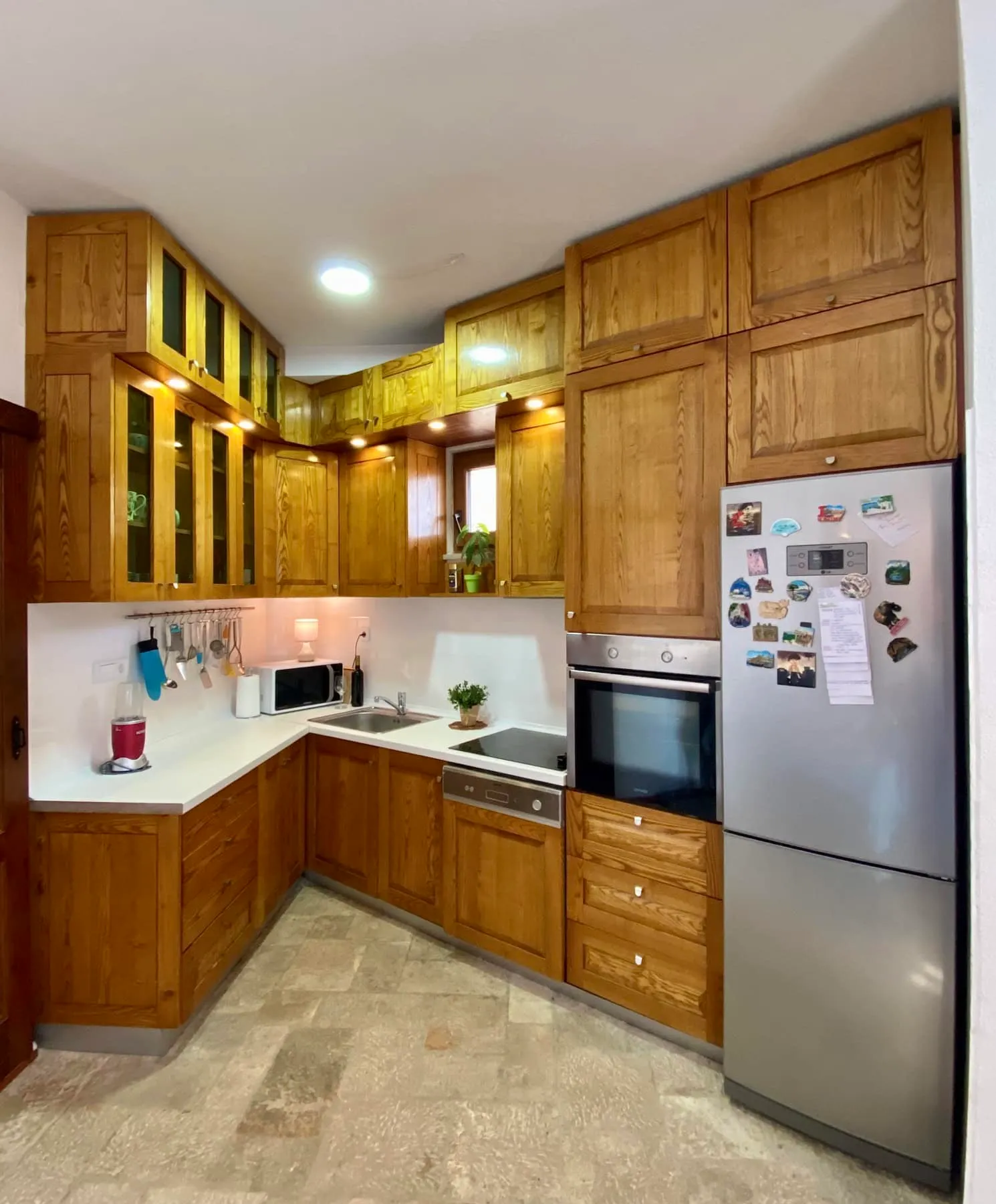 Corner kitchen made of solid wood with modern appliances in a house, Shushan, Montenegro. Light countertop and stone floor.