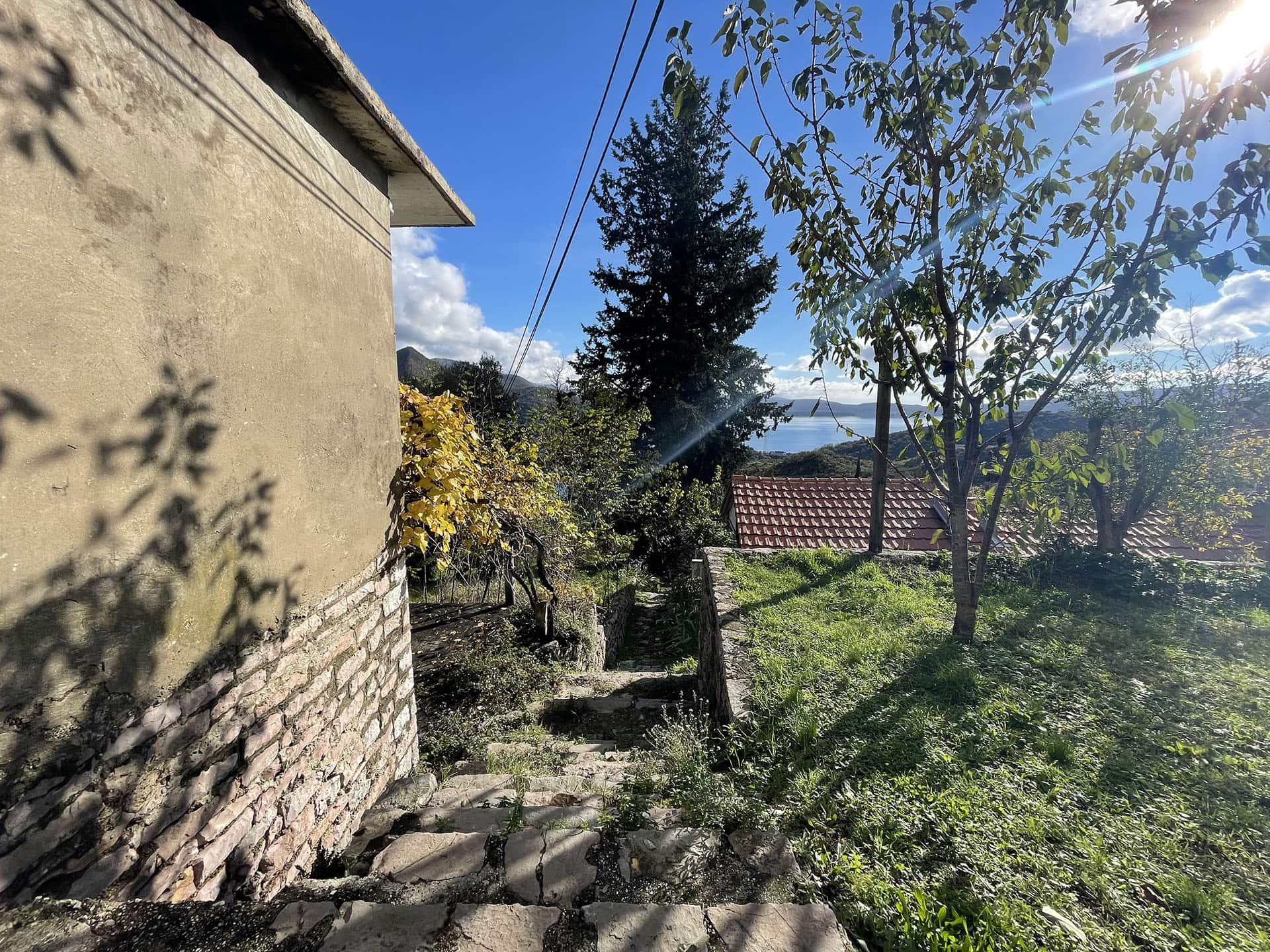 Terrain à Kamenari, Monténégro : vue sur la mer, maçonnerie en pierre de la maison et jardin avec arbres sur la pente.