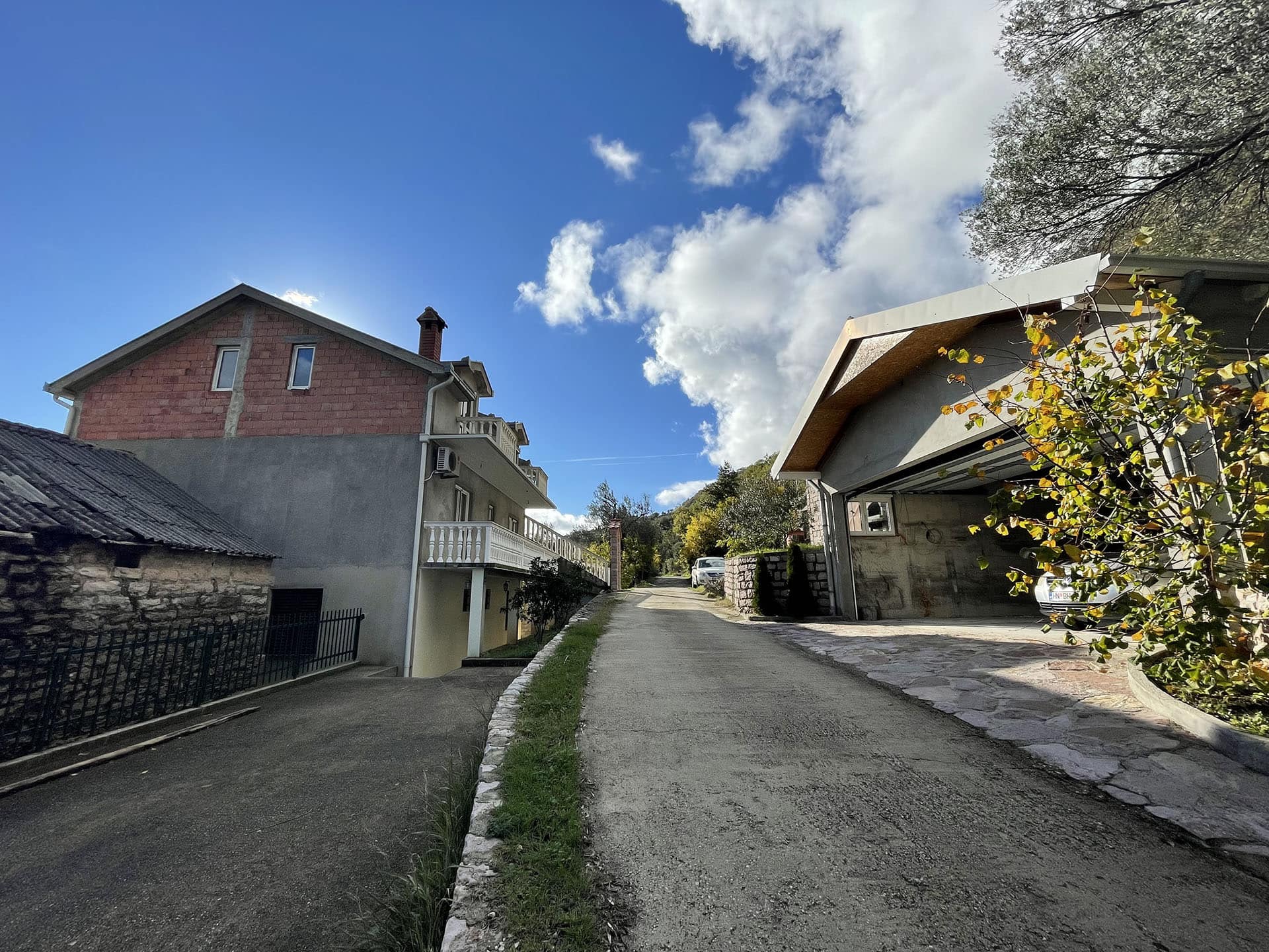 Vue sur une maison privée et un garage sur un terrain à Kamenari, Monténégro, avec une voie d’accès et un paysage montagneux.