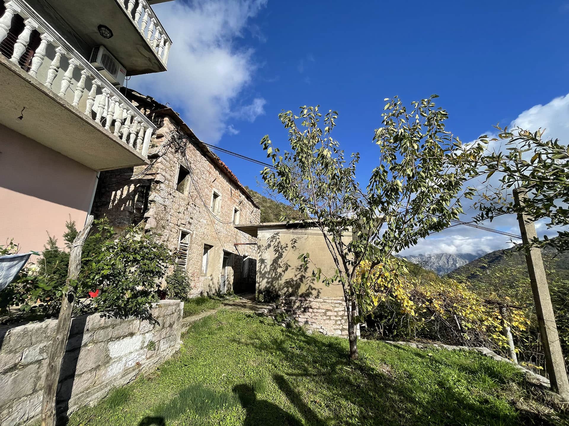 Ancienne maison en pierre sur un terrain à Kamenari, Monténégro, avec vue sur les montagnes et un jardin verdoyant autour de la maison.