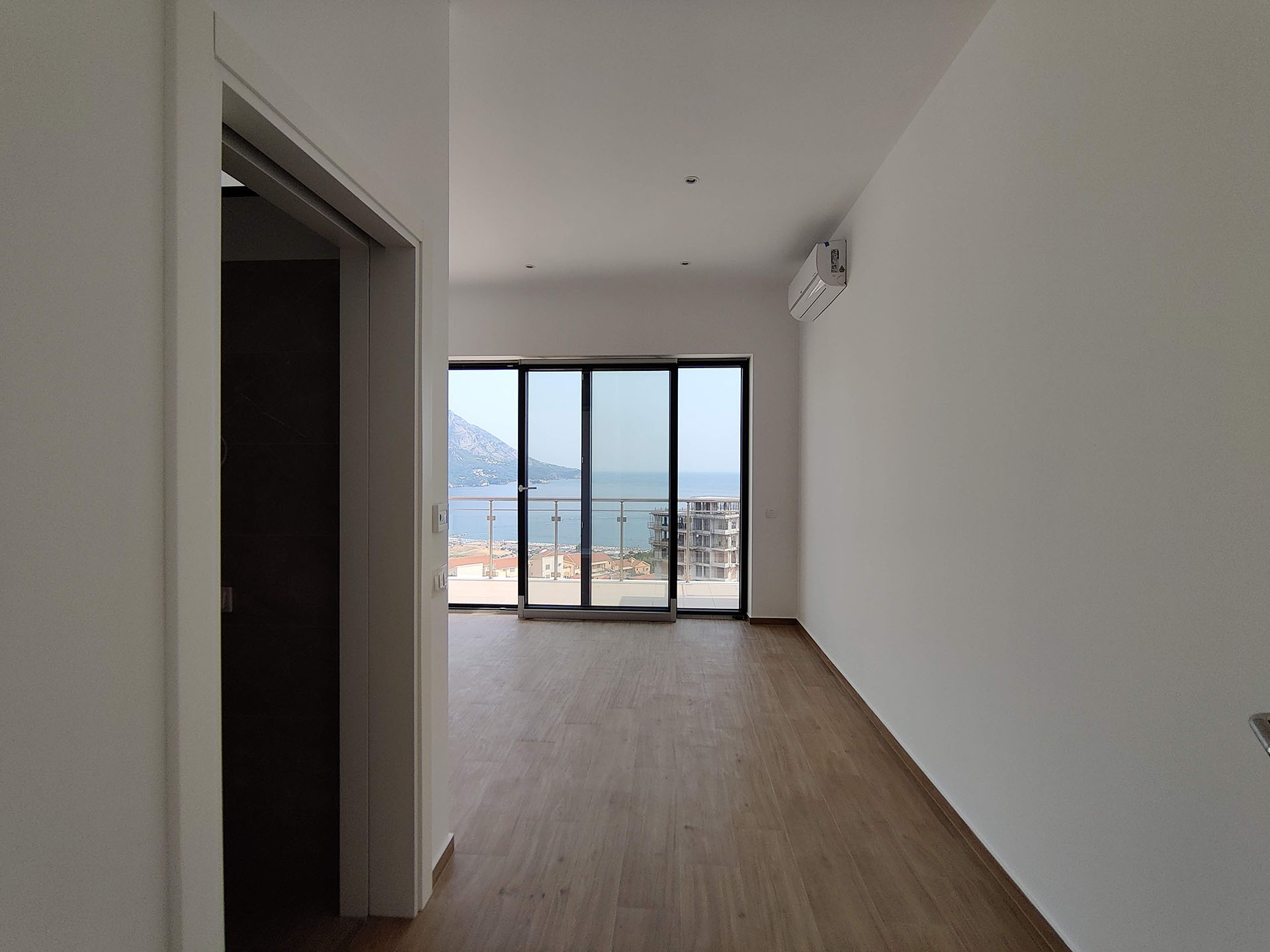 Bright living room in an apartment in Bečići, Montenegro, with panoramic sea and mountain views through the balcony door.