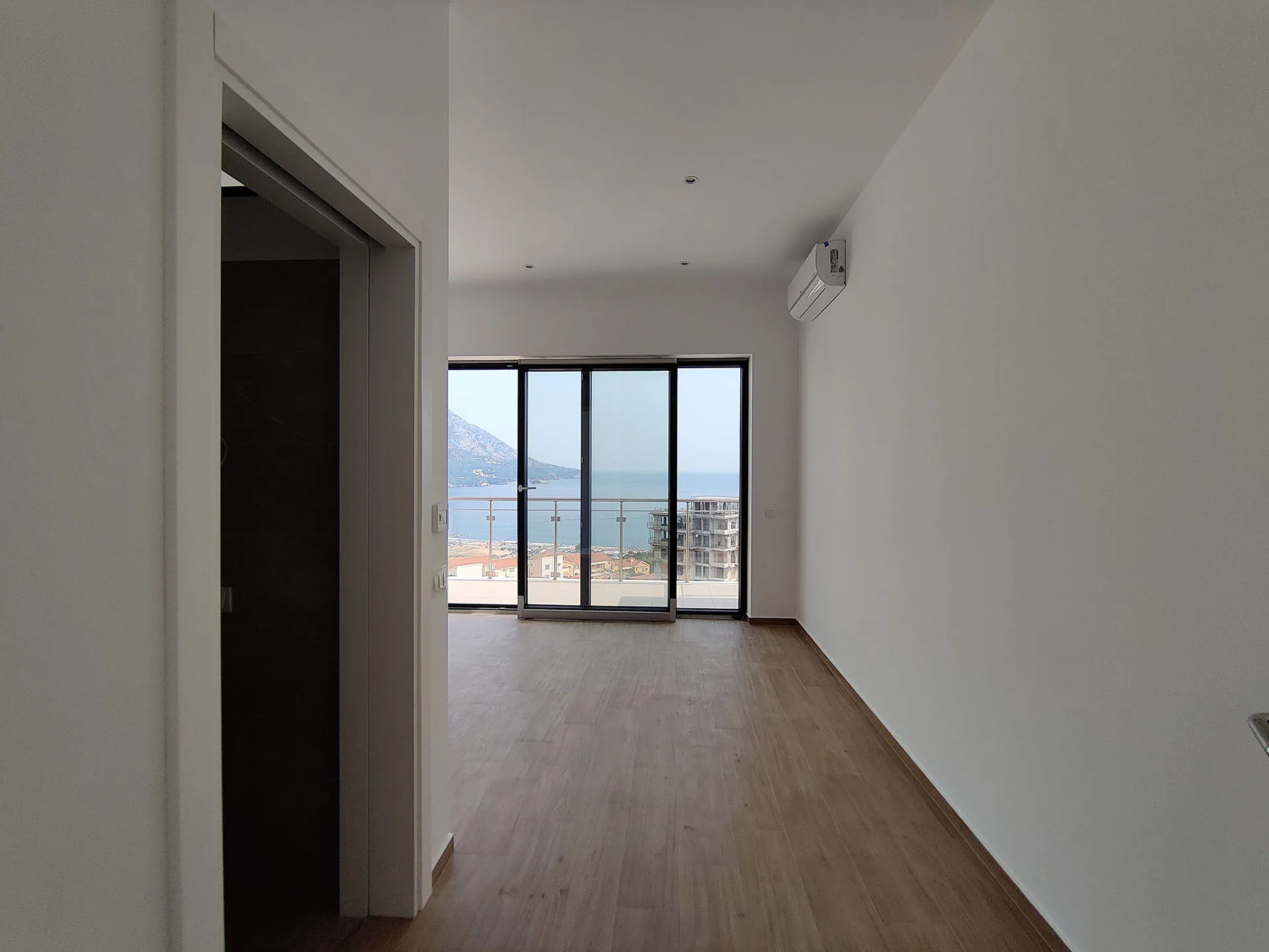 Helles Wohnzimmer in einer Wohnung in Bečići, Montenegro, mit Panoramablick auf das Meer und die Berge durch die Balkontür.