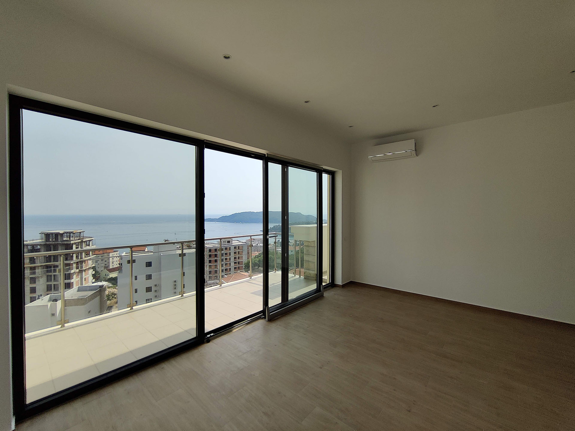 Bright living room with panoramic windows and sea view in an apartment in Becici, Montenegro, with access to a spacious terrace.
