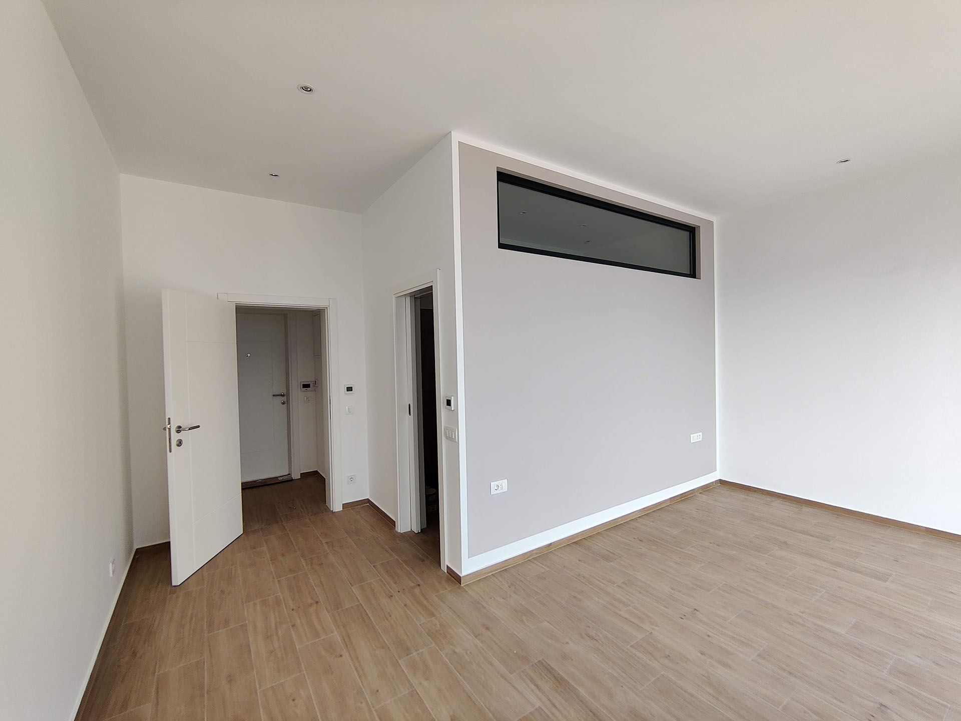 Bright living room in an apartment in Bečići, Montenegro: modern finishes, white walls, wood-look flooring, and a transom window.