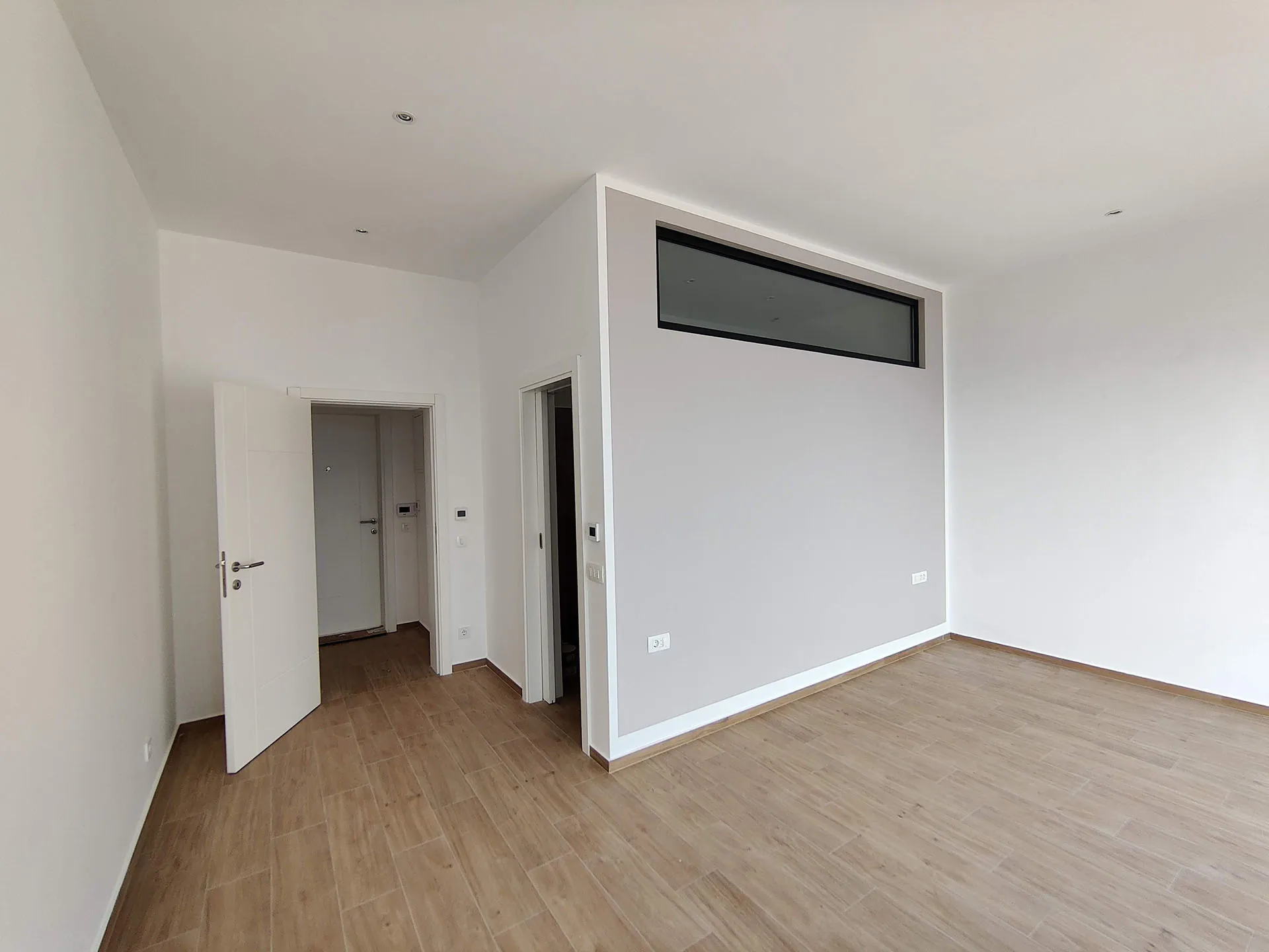 Helles Wohnzimmer in einer Wohnung in Bečići, Montenegro: moderne Ausstattung, weiße Wände, Holzoptik-Boden und Oberlicht.