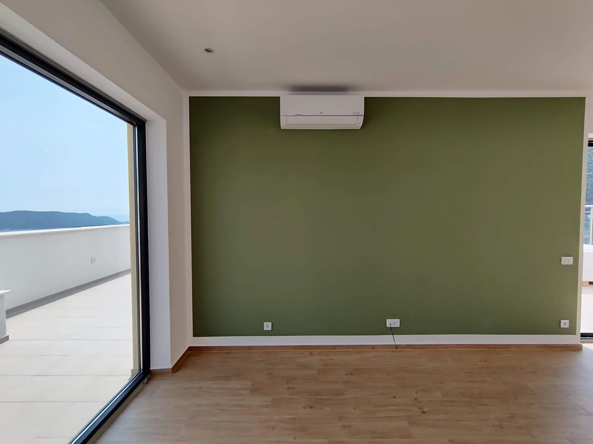 Wohnzimmer mit Panoramafenster und Meerblick in einer Wohnung, Bečići, Montenegro: grüne Wand, Parkett und Klimaanlage.