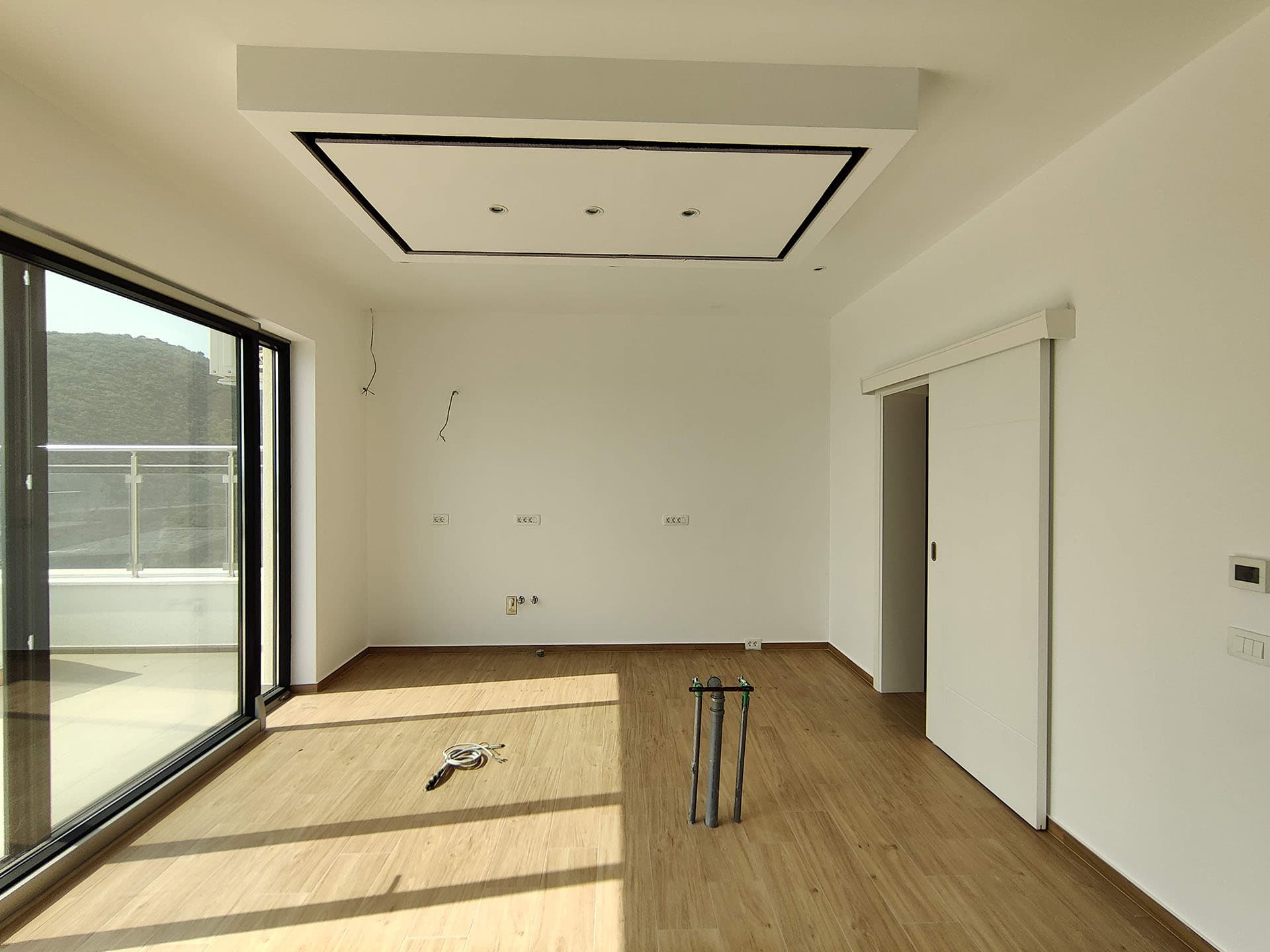 Bright living room in a new apartment in Becici, Montenegro: panoramic window, sliding door, and modern ceiling.