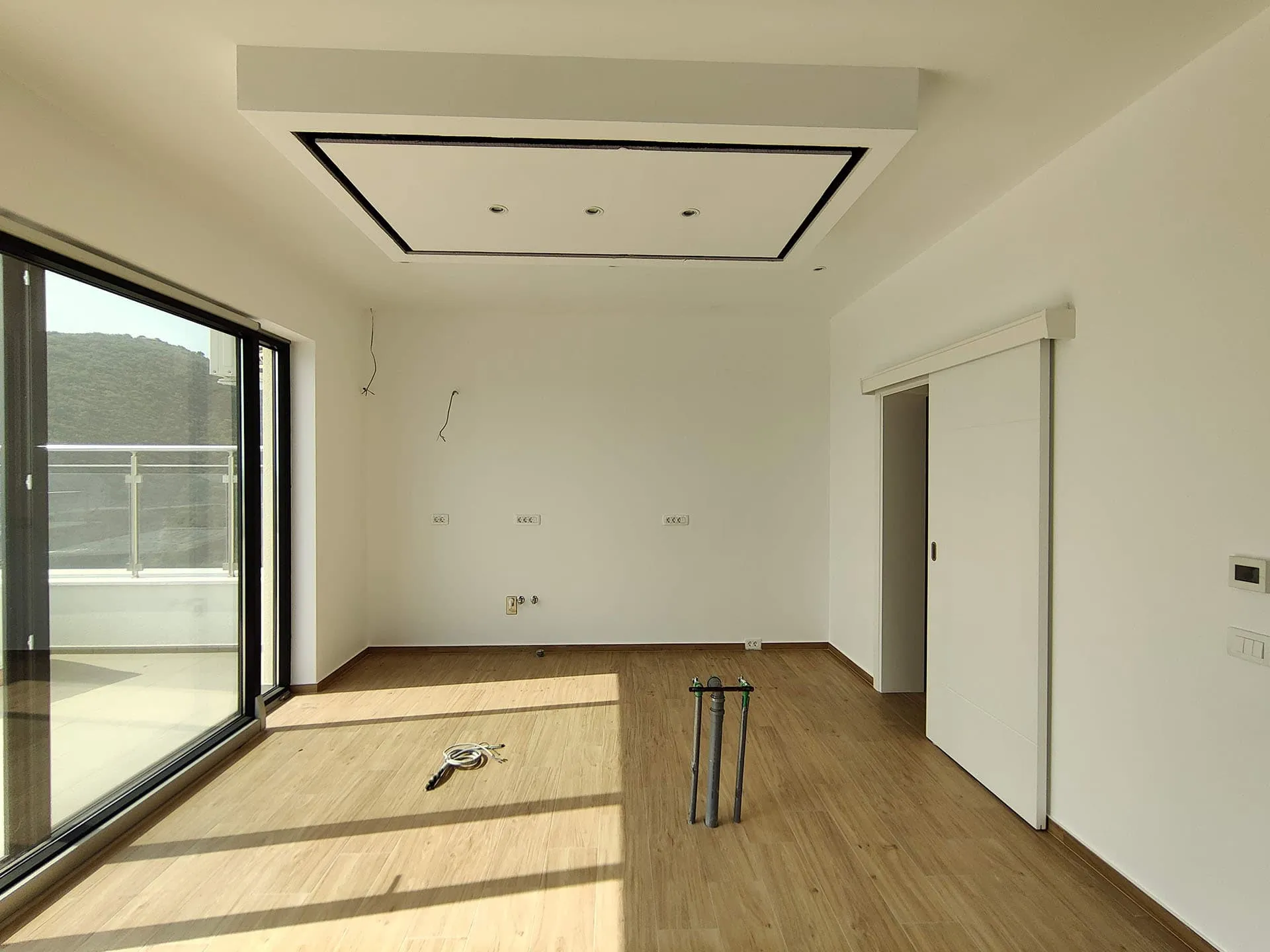 Helles Wohnzimmer in einer neuen Wohnung in Bečići, Montenegro: Panoramafenster, Schiebetür und moderne Decke.