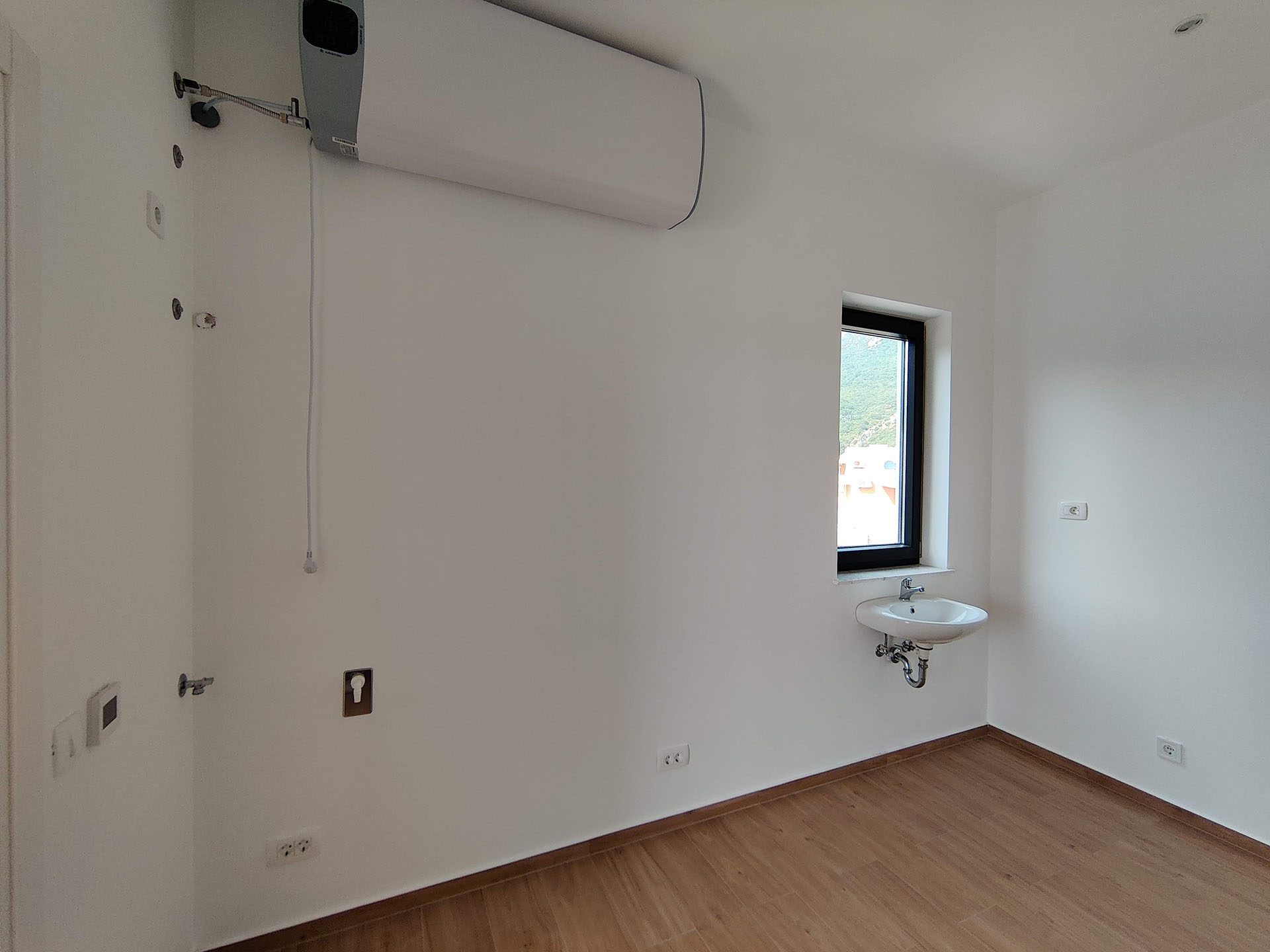 Bright bathroom in an apartment in Bečići, Montenegro: wall-mounted water heater, sink, and mountain view from the window.
