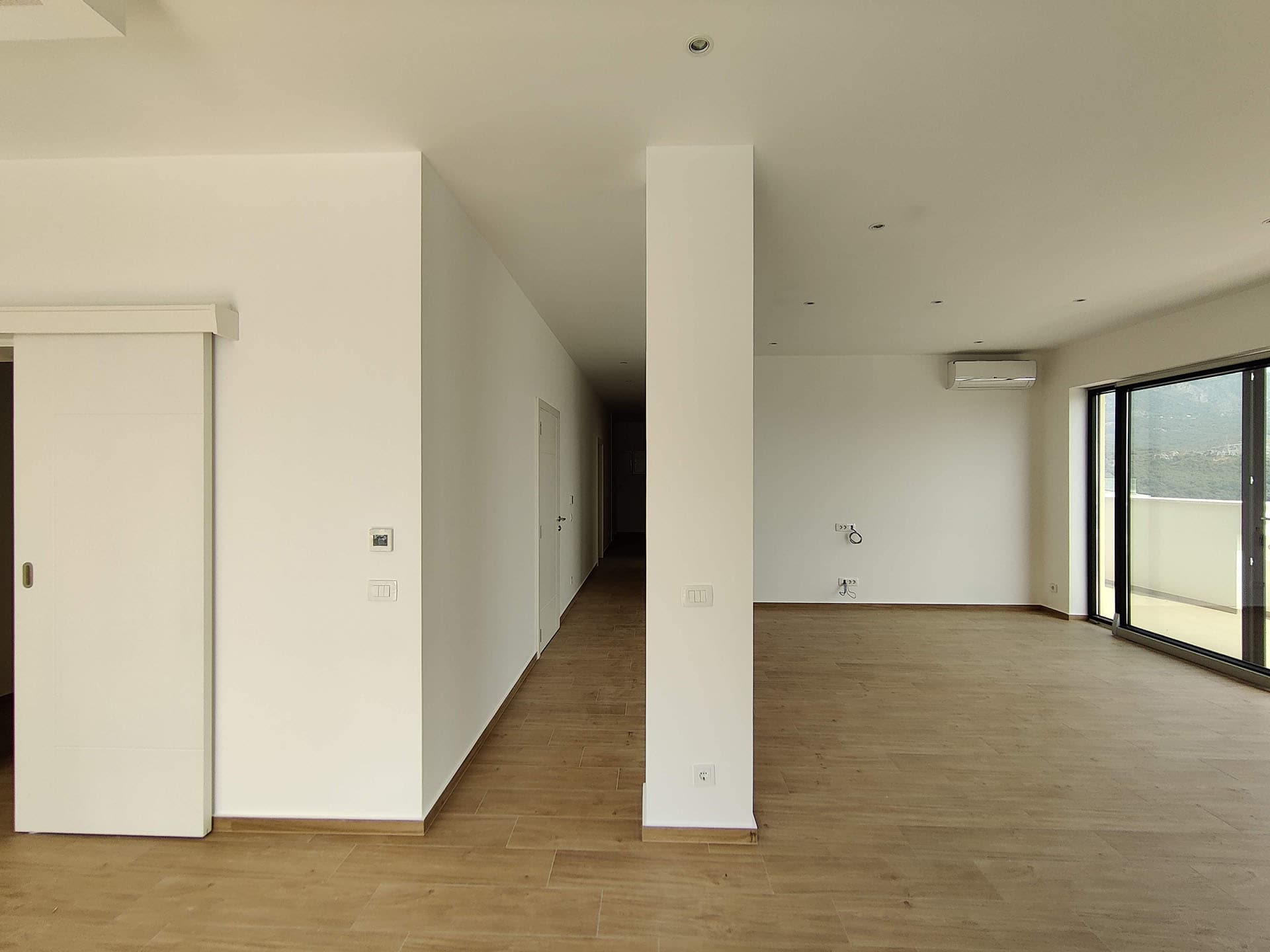 Bright living room in a modern apartment in Bečići, Montenegro: panoramic windows, light flooring, and sliding doors.