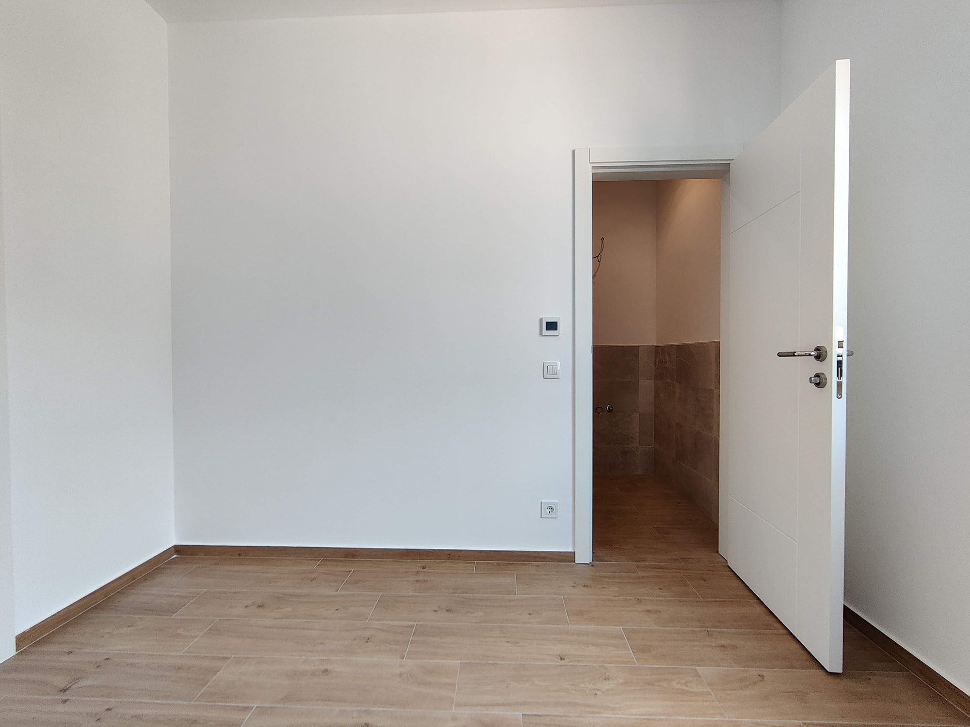 Bright room with wood finish in a new apartment in Becici, Montenegro, view of the bathroom entrance.