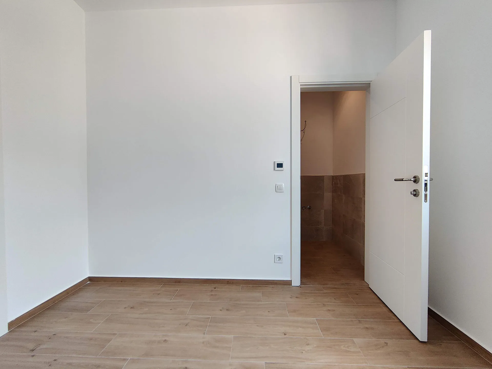 Heller Raum mit Holzverkleidung in einer neuen Wohnung in Bečići, Montenegro, Blick auf den Eingang zum Badezimmer.