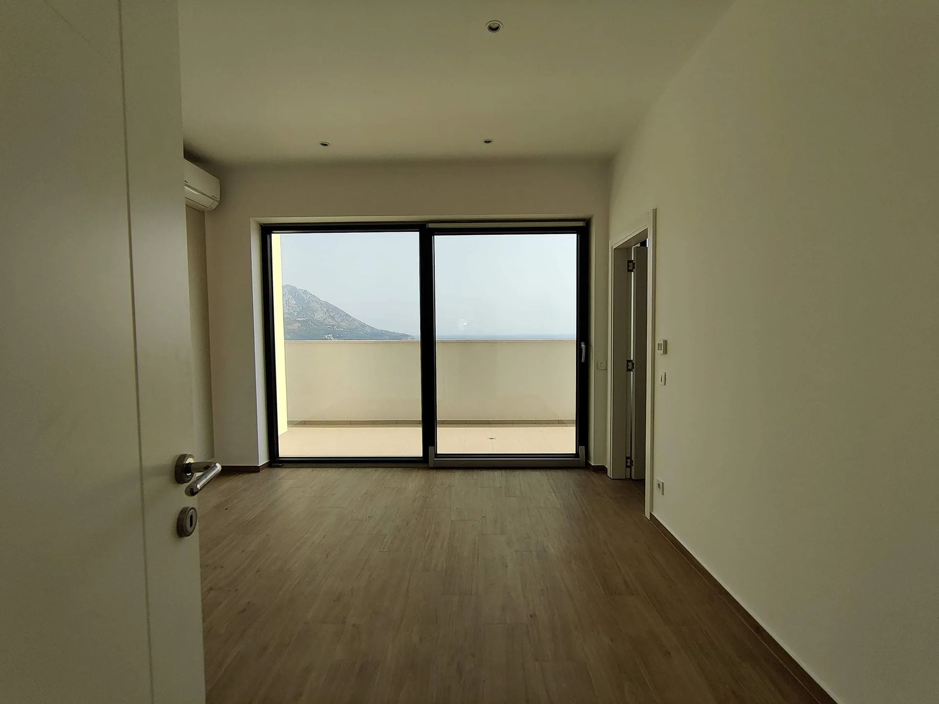 Helles Wohnzimmer in einer Wohnung in Bečići, Montenegro, mit Panoramafenster, Zugang zur Terrasse und Blick auf das Meer und die Berge.