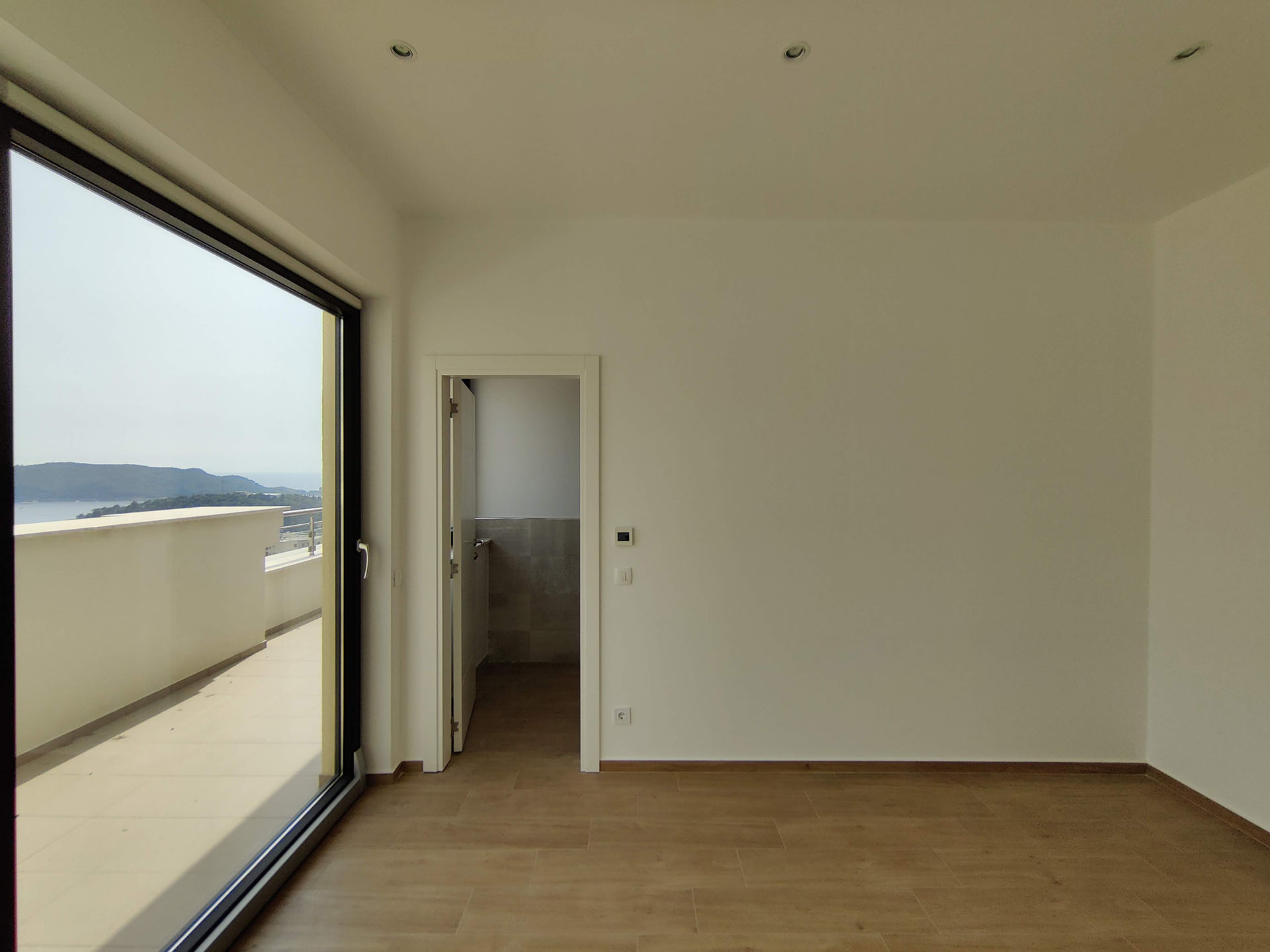 Bright living room in an apartment in Becici, Montenegro: panoramic window, access to a terrace with sea and mountain views.